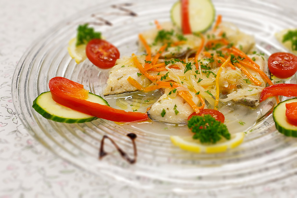 Carpaccio di pesce con verdure julienne, pomodorini e cetriolo su piatto trasparente